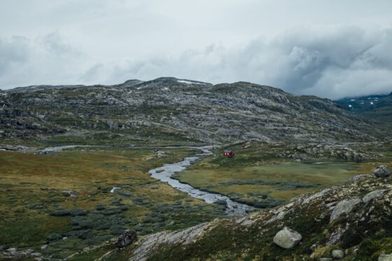 A beautiful scenery on the Rallarvegen with green mountains and a river with a little red wooden house next to it