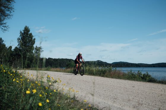 Gravel cycling in Dalsland — Sabina riding along a forest road with lake views behind her